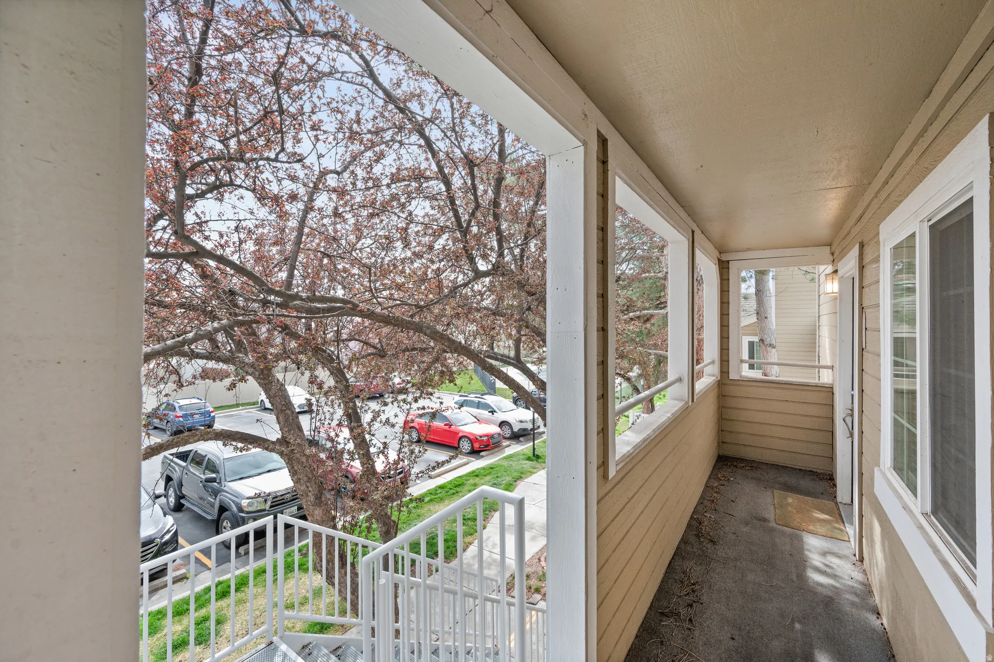 Covered exterior balcony featuring a door with a screen, windows with white trim, and light beige siding