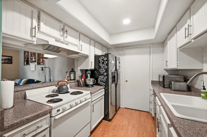 Kitchen featuring white shaker-style cabinetry, wood-finish flooring, and a subway tile backsplash