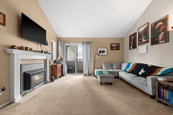 Living area featuring a fireplace with a white mantel, sliding glass doors, vaulted ceilings, and neutral-toned wall-to-wall carpeting