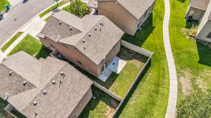 Aerial perspective showcasing a property with a fenced backyard, an exterior patio, a shingled roof, and a paved street