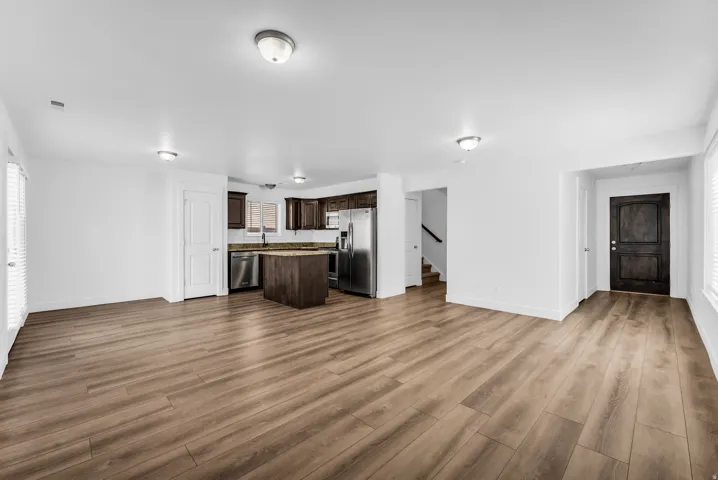 Open-concept living space featuring wood-finish flooring, a kitchen with dark cabinetry, stainless steel appliances, and a central island with a stone countertop