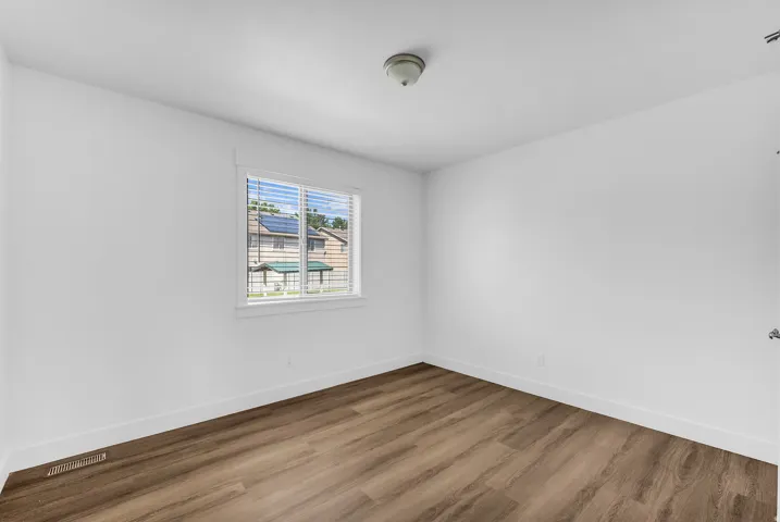 Room featuring wood-finish flooring, white walls, and a window with horizontal blinds