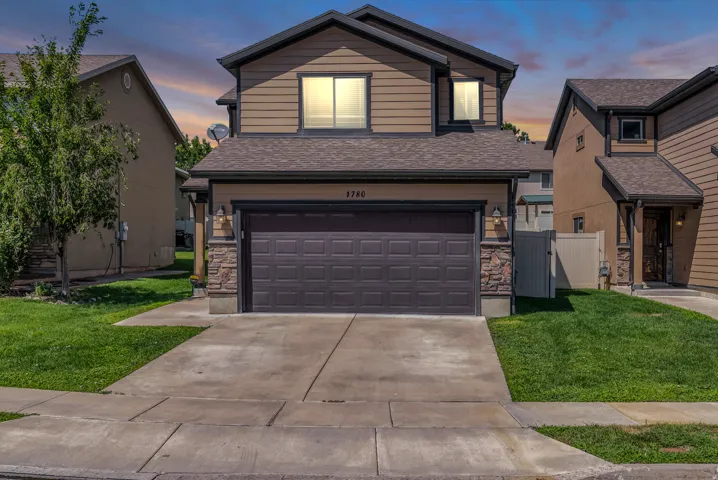 Two-story home featuring a charcoal gray garage door with panel detailing, stone veneer accents flanking the garage opening, and a poured concrete driveway