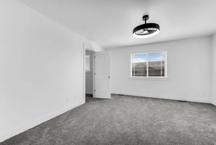 Spacious bedroom featuring neutral carpeting, white walls, and abundant natural light from a large window with plantation shutters