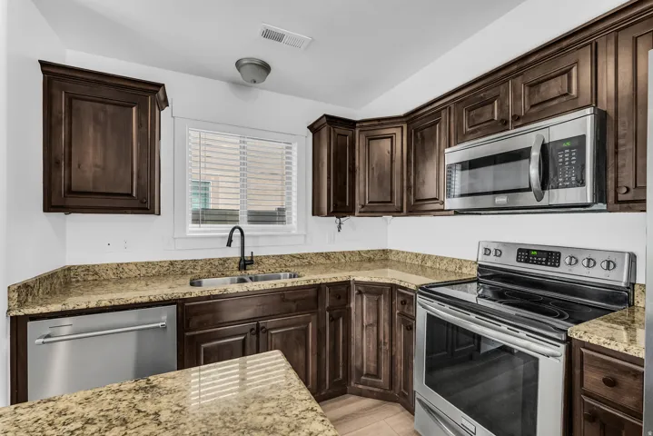 Kitchen featuring dark wood cabinetry, light-toned countertops, stainless steel appliances, and a window with blinds