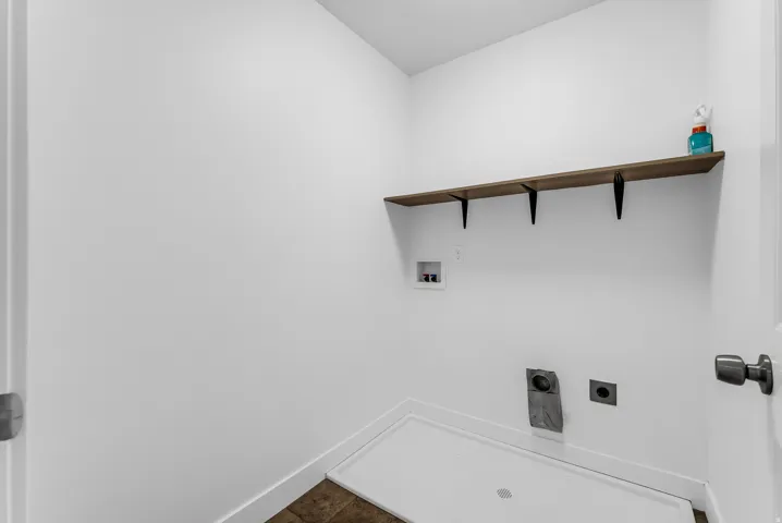 Dedicated laundry area featuring a wood-finish shelf with black brackets, white walls, and a utility pan