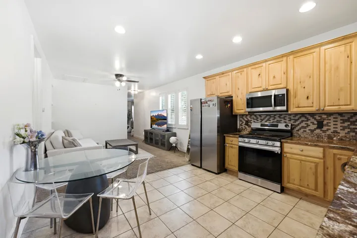 Open-concept kitchen and living area featuring stainless steel appliances, wood cabinetry, patterned tile backsplash, and recessed lighting
