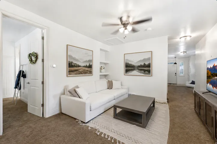 Bright, open-concept living area featuring neutral wall finishes, a ceiling fan with integrated lighting, and wood-finish flooring throughout