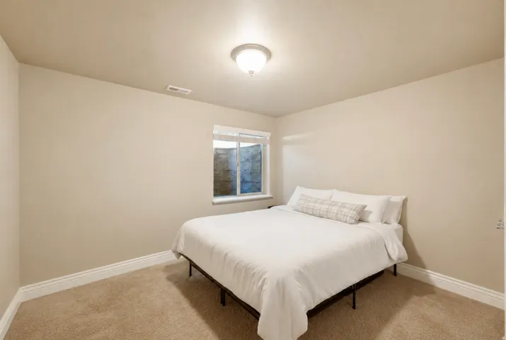 Bright bedroom featuring neutral wall finishes, carpeted flooring, and a large window allowing natural light
