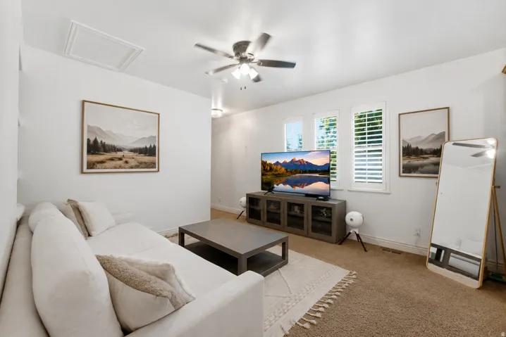 Bright, open living room featuring neutral wall finishes, ceiling fan with integrated lighting, and wood-finish flooring throughout