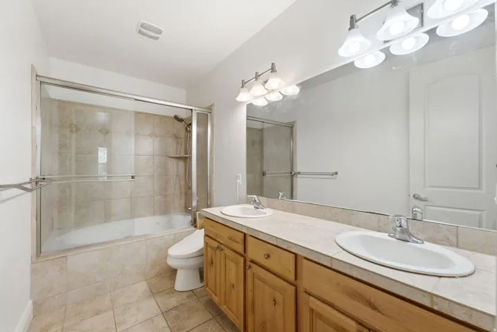 Spa-inspired master bathroom featuring dual vanity with wood-finish cabinetry, white countertop, and polished chrome fixtures