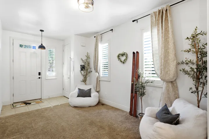 Bright and airy entryway with neutral carpet flooring, white shaker-style entry door with sidelights, and multiple windows featuring plantation shutters and natural light