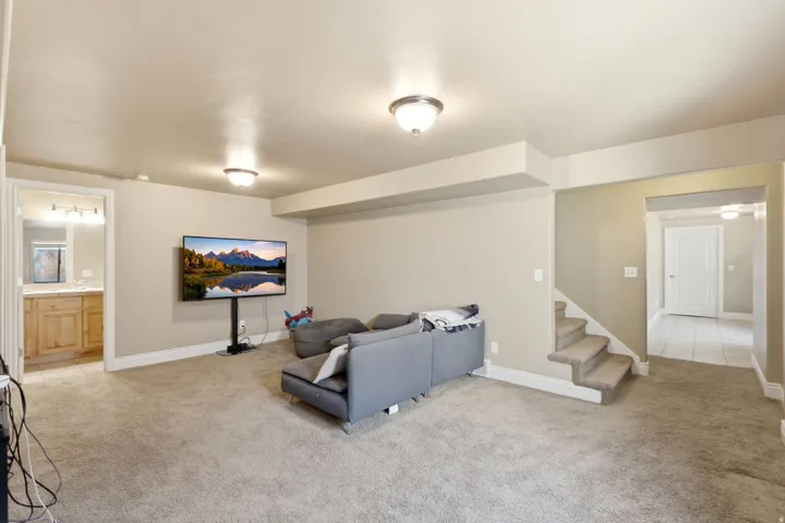 Carpeted entertainment area featuring recessed lighting, a doorway to a bathroom with a wood-finish vanity, and a carpeted staircase
