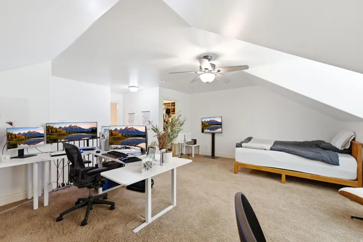 Bright attic bedroom suite featuring sloped ceilings, ceiling fan, and abundant natural light from multiple windows