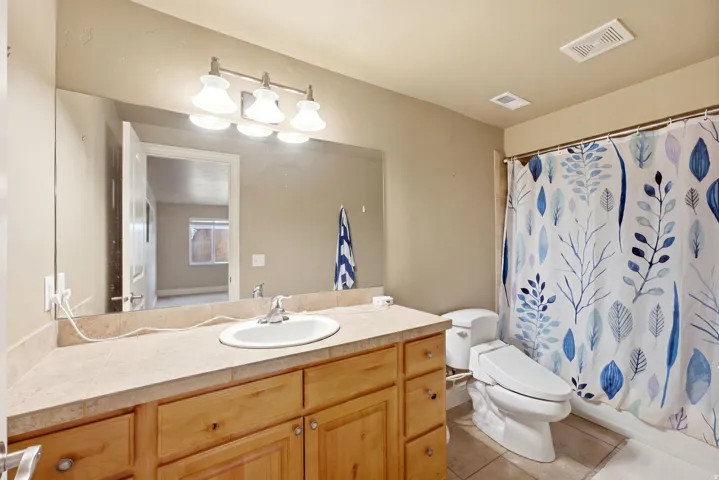 Bathroom featuring a light wood-finish vanity with a single basin sink, a large wall-mounted mirror, and a full bathtub with shower