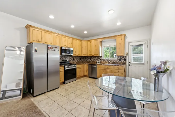 Kitchen featuring light wood cabinetry, stainless steel appliances, tile flooring, and a patterned tile backsplash