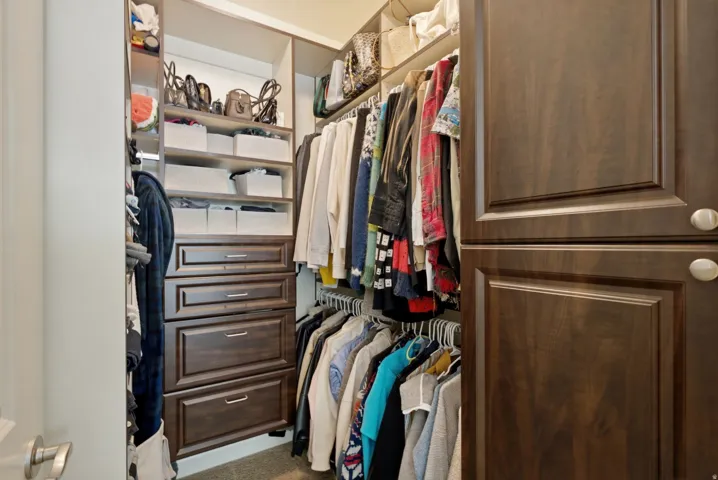 Spacious walk-in closet featuring custom wood-finish cabinetry with multiple drawers, adjustable shelving throughout, and a double hanging rod system for organized clothing storage