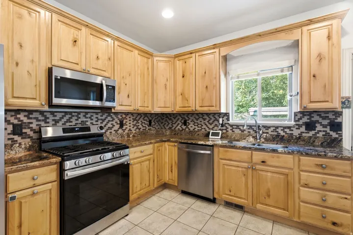 Kitchen featuring wood cabinetry, stainless steel appliances, patterned tile backsplash, and stone-finish countertops