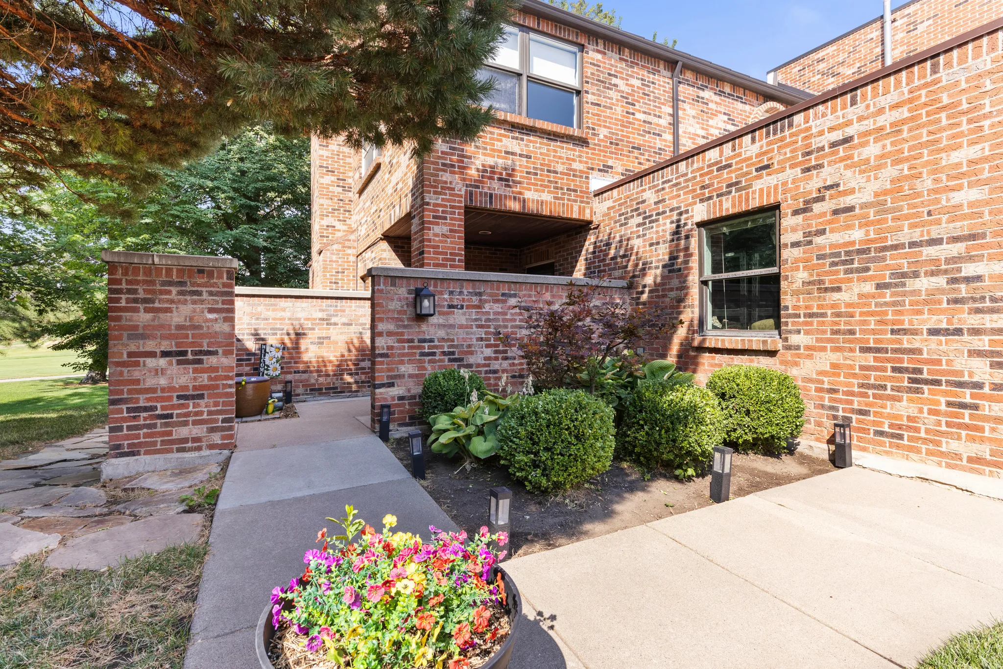 Welcoming brick exterior with mature landscaping, manicured hedges, and vibrant seasonal plantings
