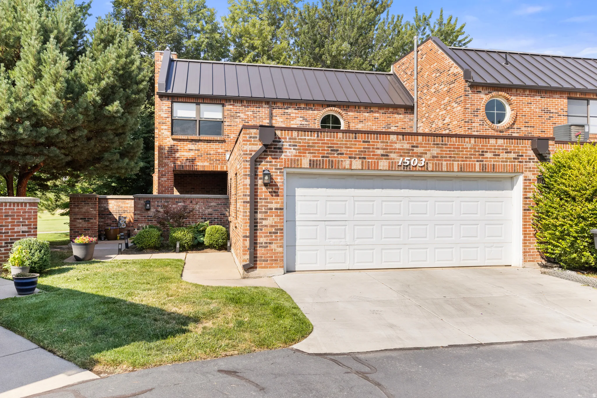 Brick exterior with a metal roof, an integrated two-car garage, and round architectural windows