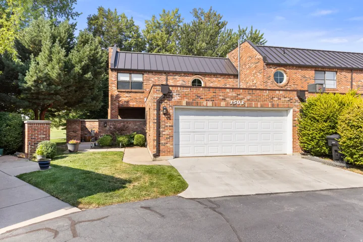 Brick exterior with a metal roof, featuring a two-car garage, circular windows, and a manicured lawn
