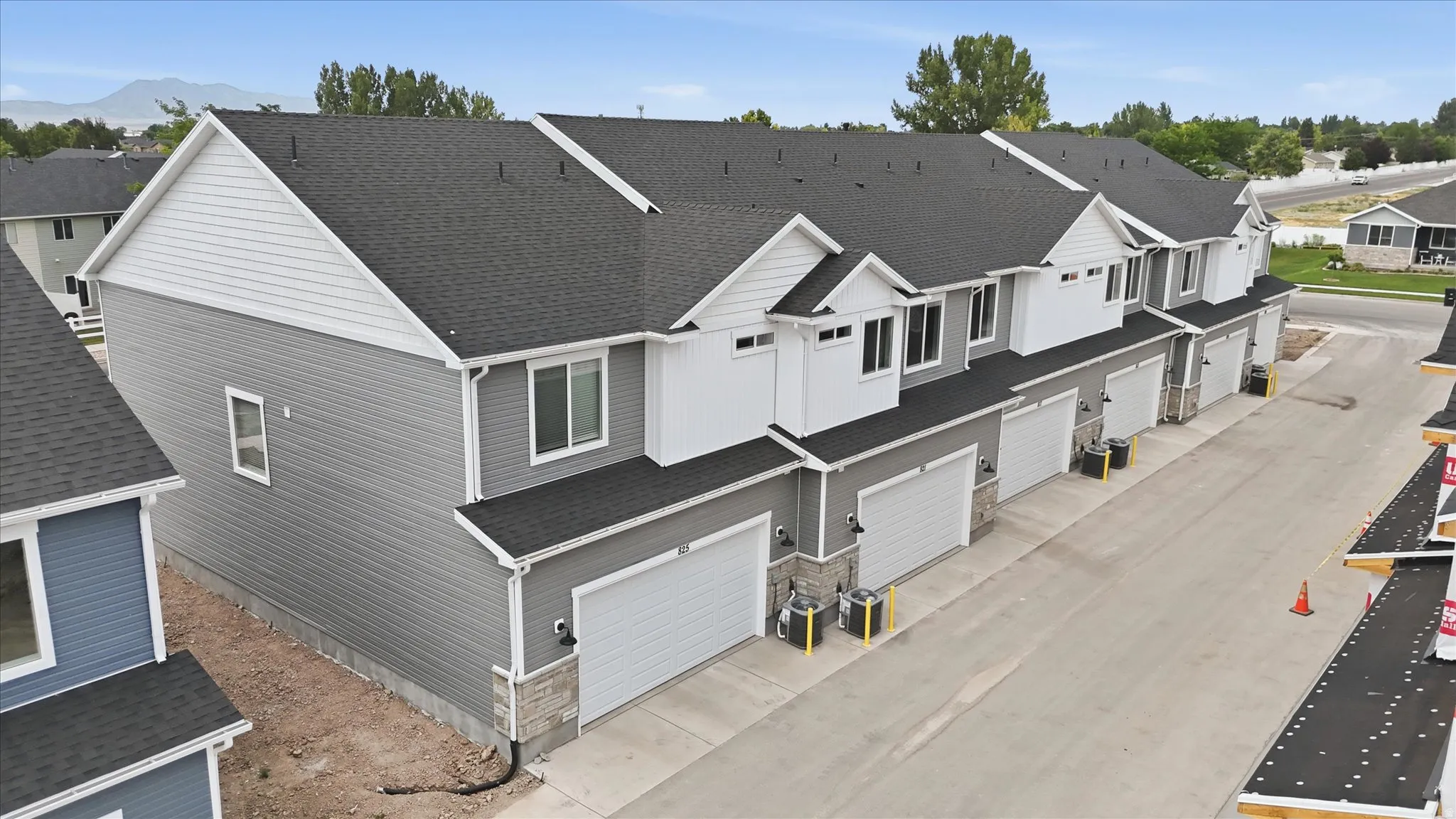 Newly constructed townhome community with attached garages, gray siding, stone accents, and dark shingle roofs