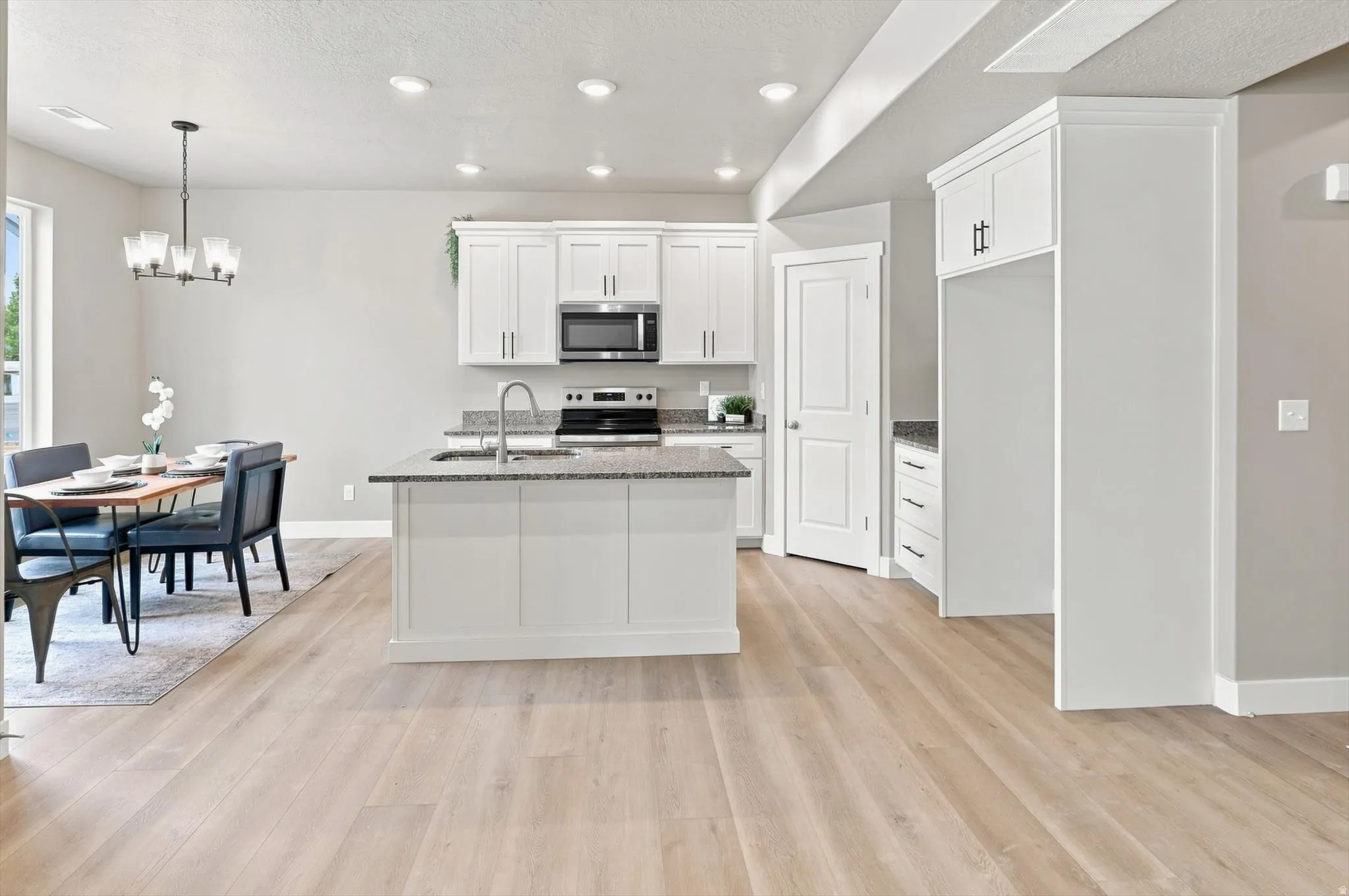 Open-concept kitchen and dining area featuring white cabinetry, stainless steel appliances, granite countertops, a large center island with seating, and wide-plank wood-finish flooring throughout