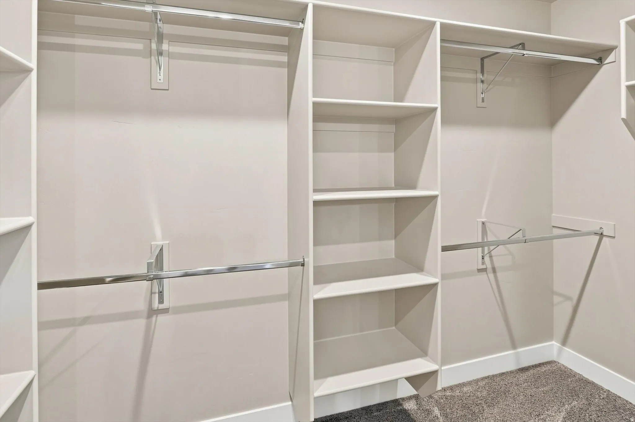 Spacious walk-in closet featuring dual clothing rods, extensive shelving throughout, pendant lighting, and carpeted flooring
