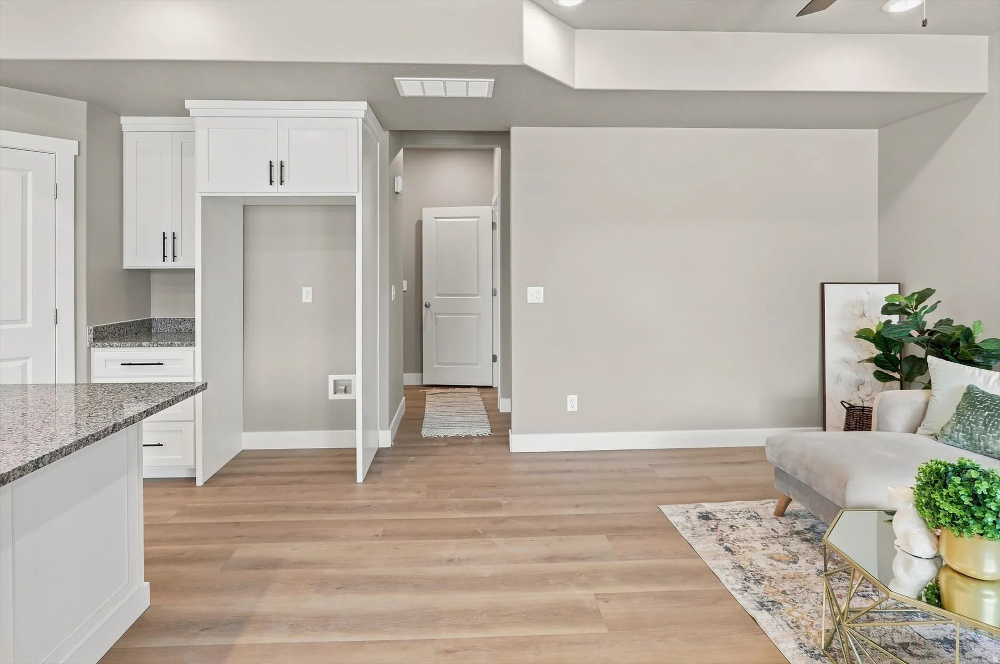 Open-concept living space featuring warm wood-finish flooring throughout, white cabinetry with brushed nickel hardware, granite countertops, and recessed ceiling lighting