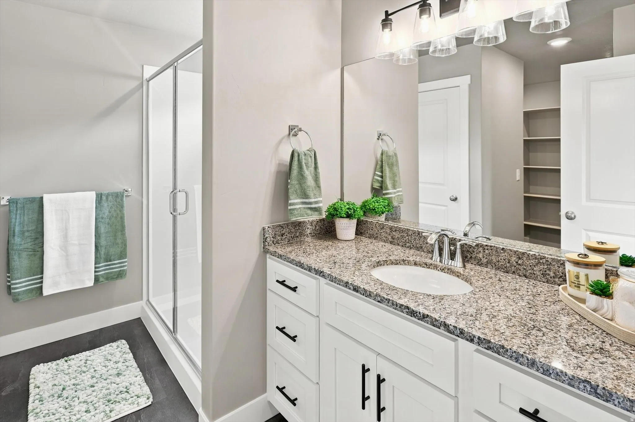 Spa-inspired primary bathroom featuring dual vanities with stone countertops, white cabinetry with integrated hardware, and a frameless glass-enclosed shower