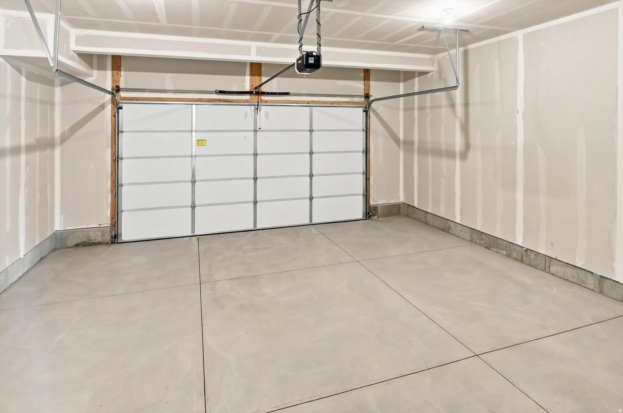 Spacious garage featuring a sectional overhead door with multiple panels, concrete flooring with control joints, and overhead mechanical systems including a pulley-operated opener and structural framing
