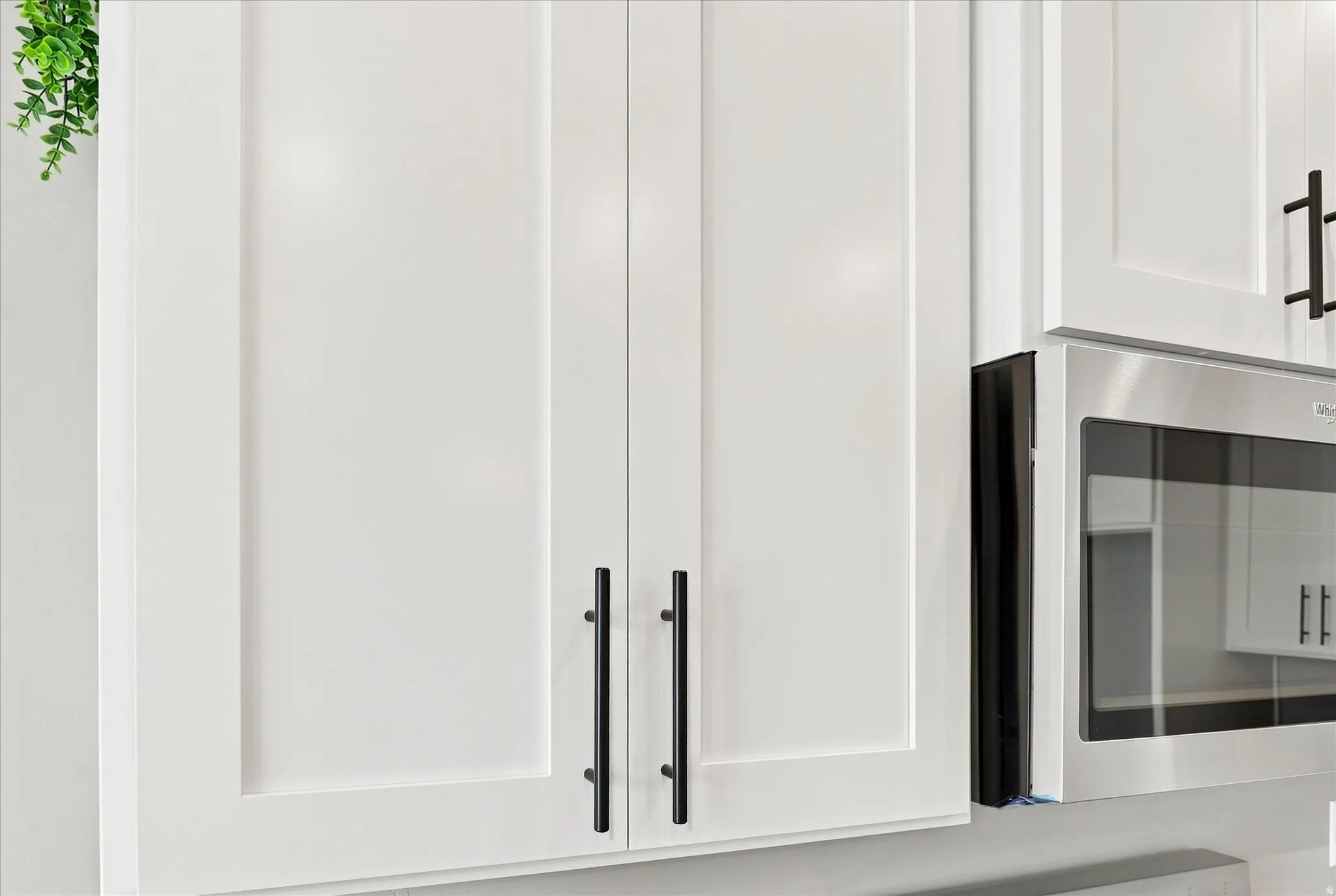 Modern kitchen cabinetry featuring crisp white shaker-style doors with sleek black hardware and stainless steel appliances, including a built-in microwave