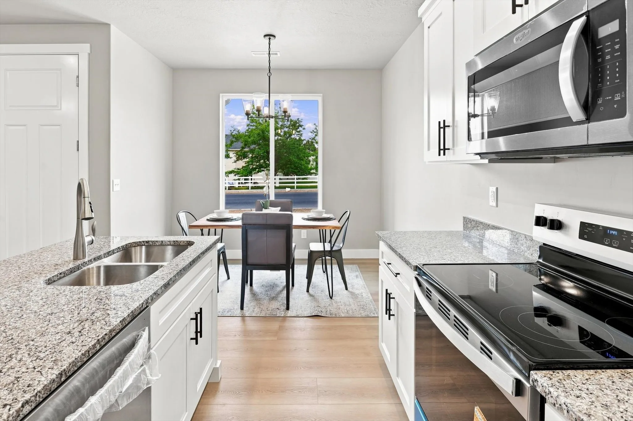 Galley-style kitchen featuring stainless steel appliances, including a built-in microwave and dual wall ovens, quartz countertops, white cabinetry with hardware accents, an undermount sink, and hardwood flooring throughout