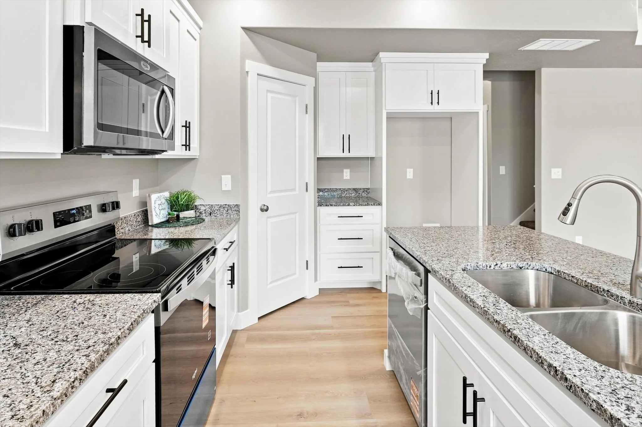 White cabinetry, granite countertops, stainless steel appliances, wood-finish flooring, and a double basin sink