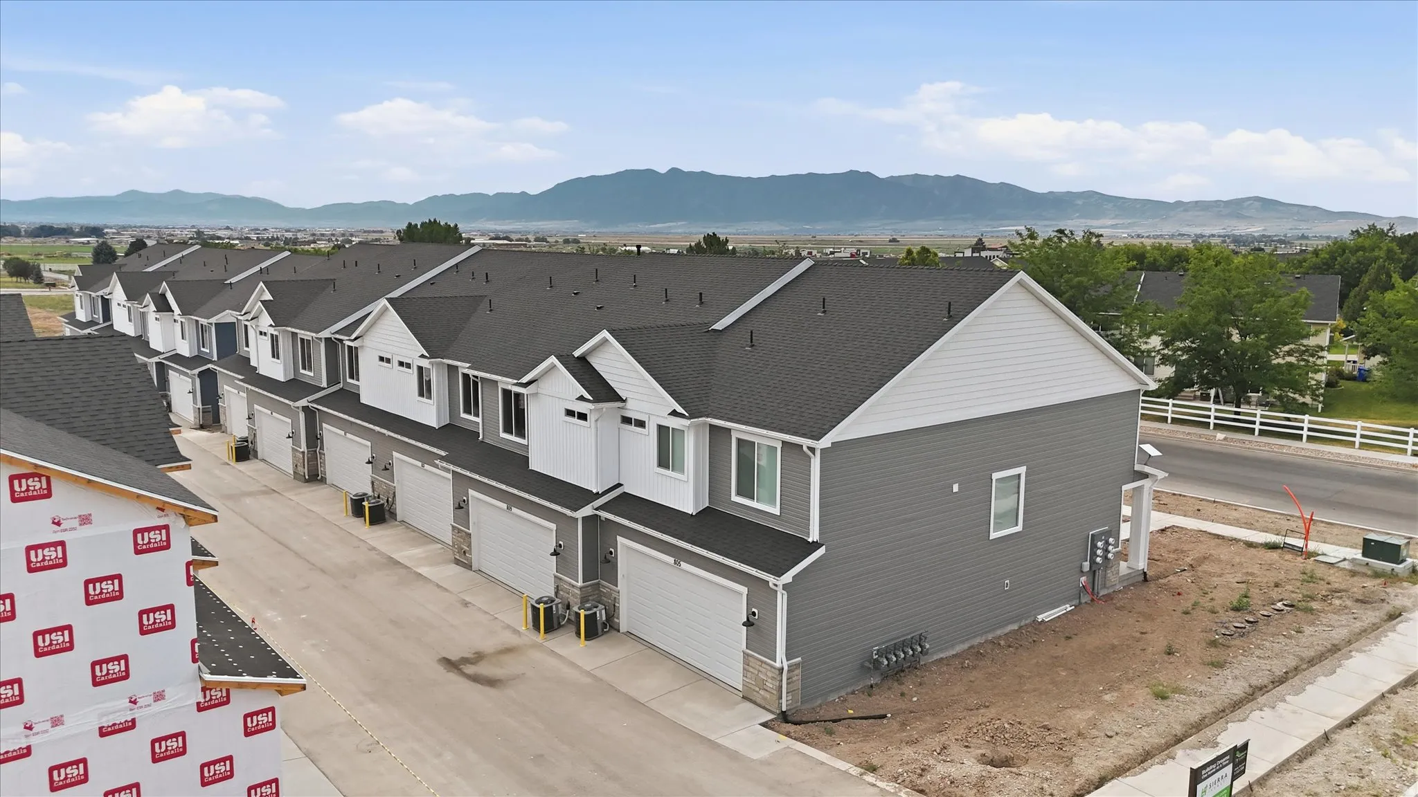 Row of newly constructed townhomes with dark gray siding, white trim, attached garages, and a mountain backdrop