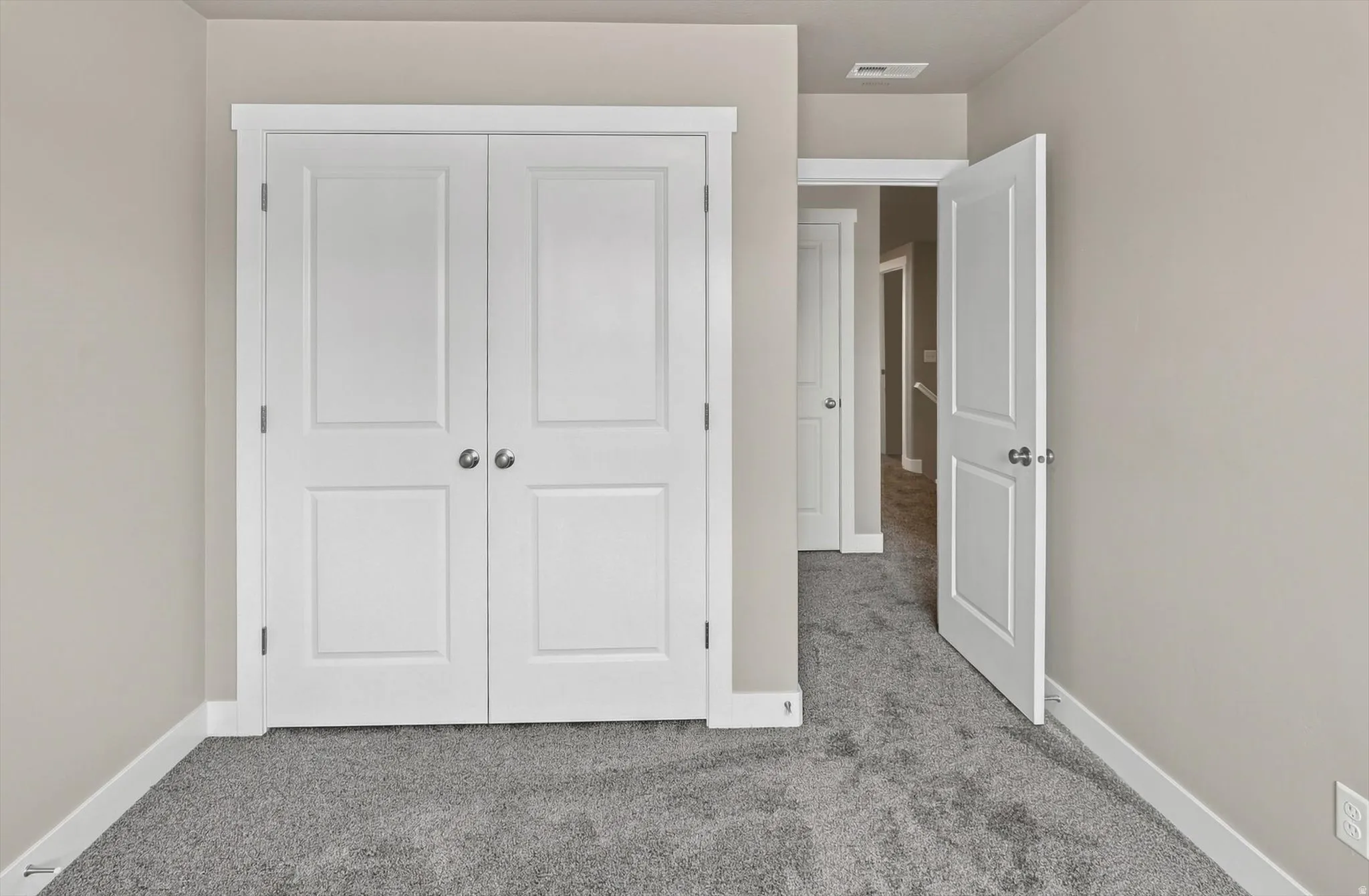 Spacious bedroom featuring dual white panel closets with brushed nickel hardware, neutral wall finishes, and soft-gray carpeting throughout