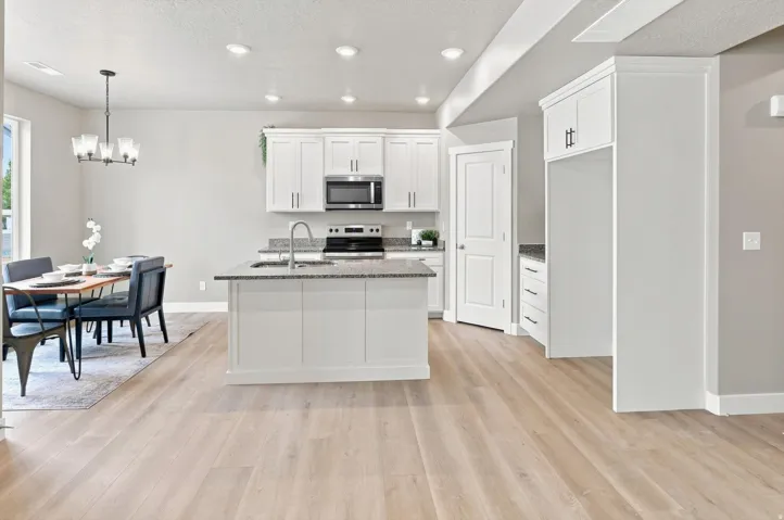 Open-concept kitchen and dining area featuring white cabinetry, stainless steel appliances, granite countertops, a large center island with seating, and wide-plank wood-finish flooring throughout