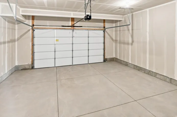Spacious garage featuring a sectional overhead door with multiple panels, concrete flooring with control joints, and overhead mechanical systems including a pulley-operated opener and structural framing