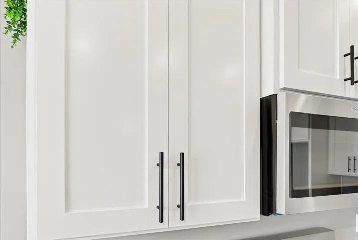 Modern kitchen cabinetry featuring crisp white shaker-style doors with sleek black hardware and stainless steel appliances, including a built-in microwave