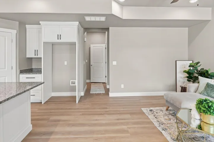 Open-concept living space featuring warm wood-finish flooring throughout, white cabinetry with brushed nickel hardware, granite countertops, and recessed ceiling lighting