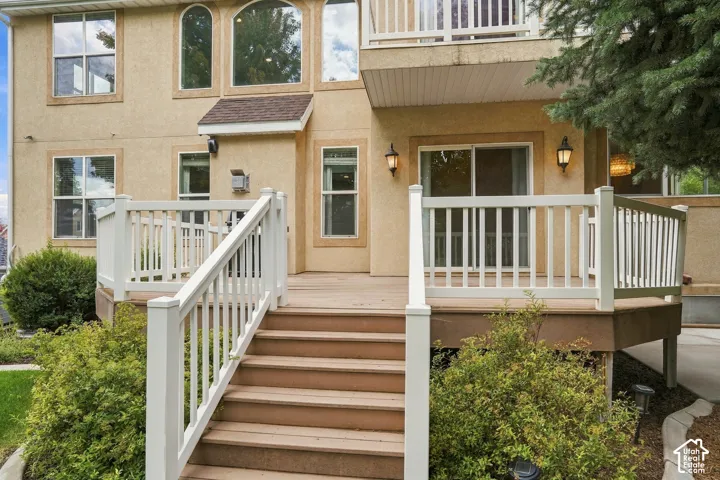 Expansive rear deck with white railing, exterior wall sconces, sliding glass door, and a second-story balcony