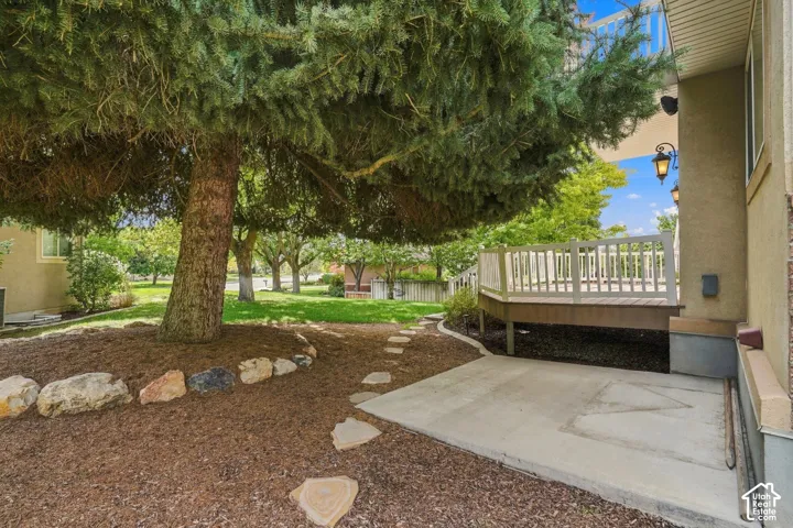 Expansive outdoor space featuring a mature tree with wood chip landscaping, a stone-lined garden bed, a multi-level wood deck with white railings, and a concrete patio