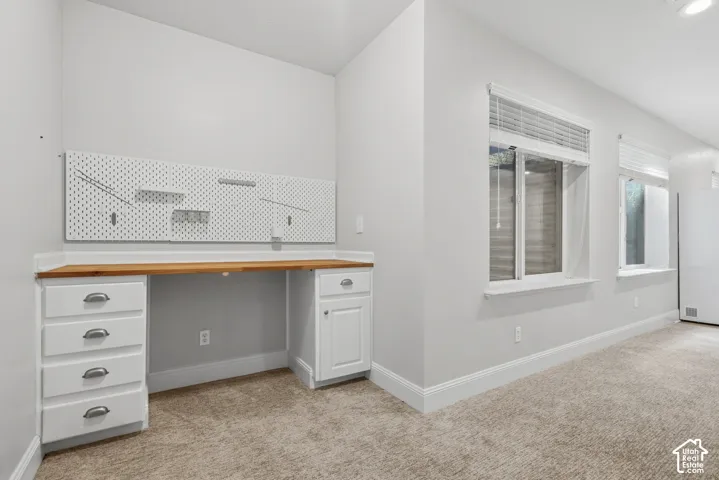 Built-in desk with wood-finish countertop, white cabinetry with silver hardware, and integrated pegboard wall