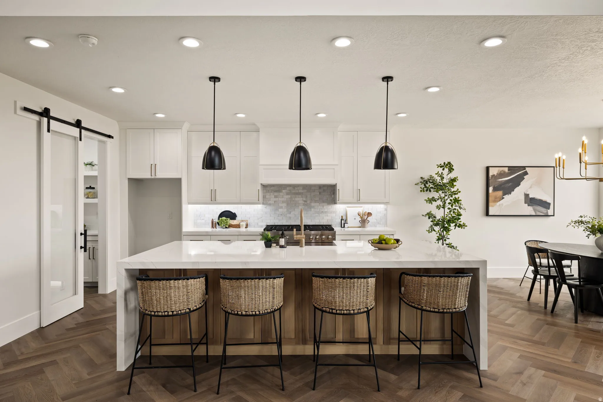 Kitchen featuring a large island with a light-toned countertop, pendant lighting, herringbone wood-finish flooring, white cabinetry, and a tile backsplash