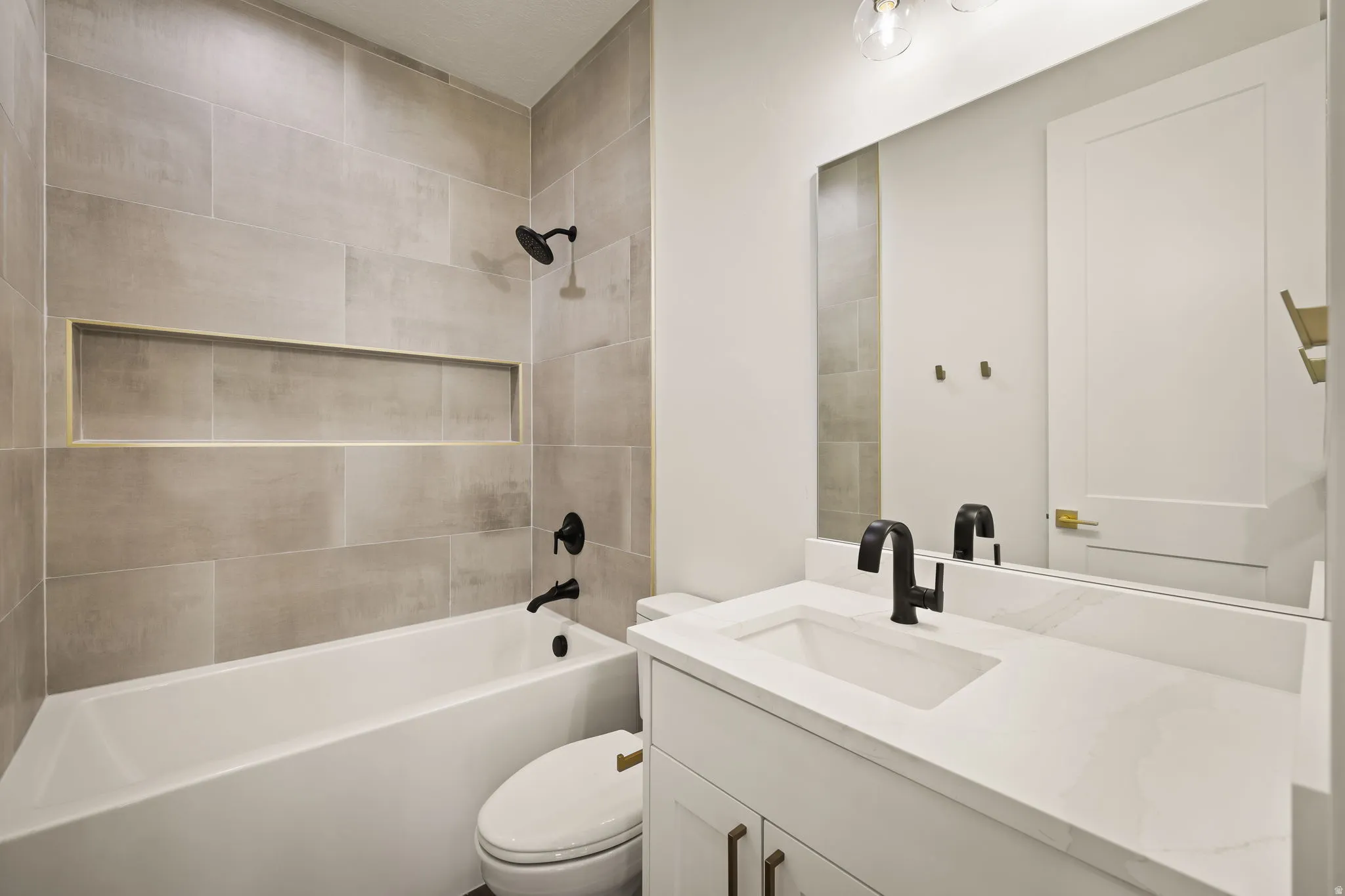 Bathroom featuring a white tub, light-toned tile surround with an integrated niche, matte black fixtures, a single vanity with a white countertop and undermount sink, and a large wall mirror
