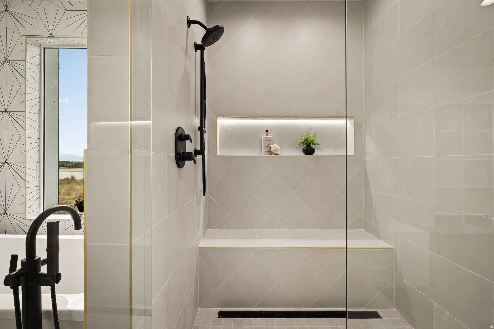 Walk-in shower with full-height glass enclosure, matte black shower fixtures, integrated bench seating, and an illuminated recessed niche