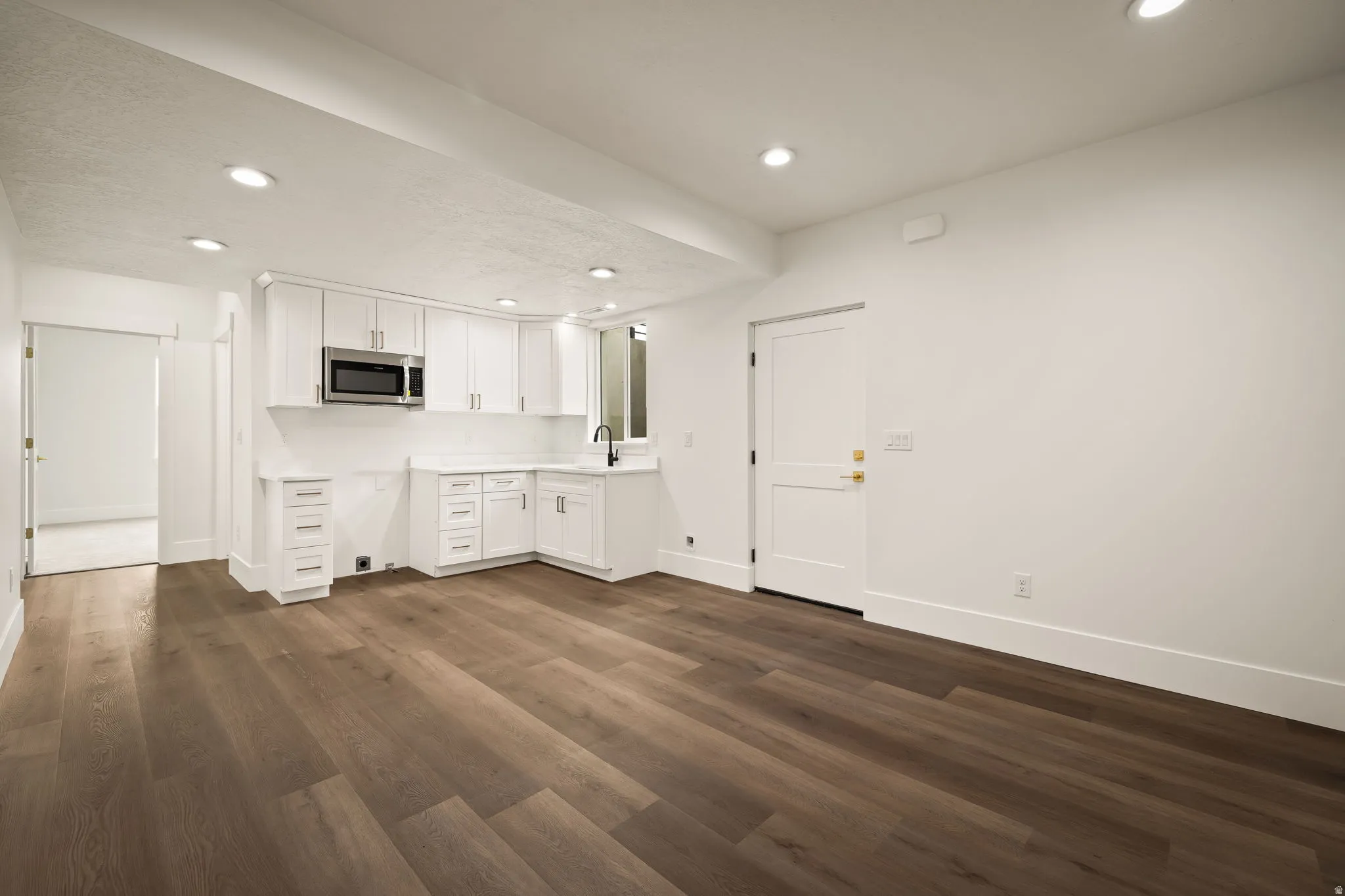 Open concept space featuring a corner kitchen with white shaker cabinetry, an undermount sink, and stainless steel microwave