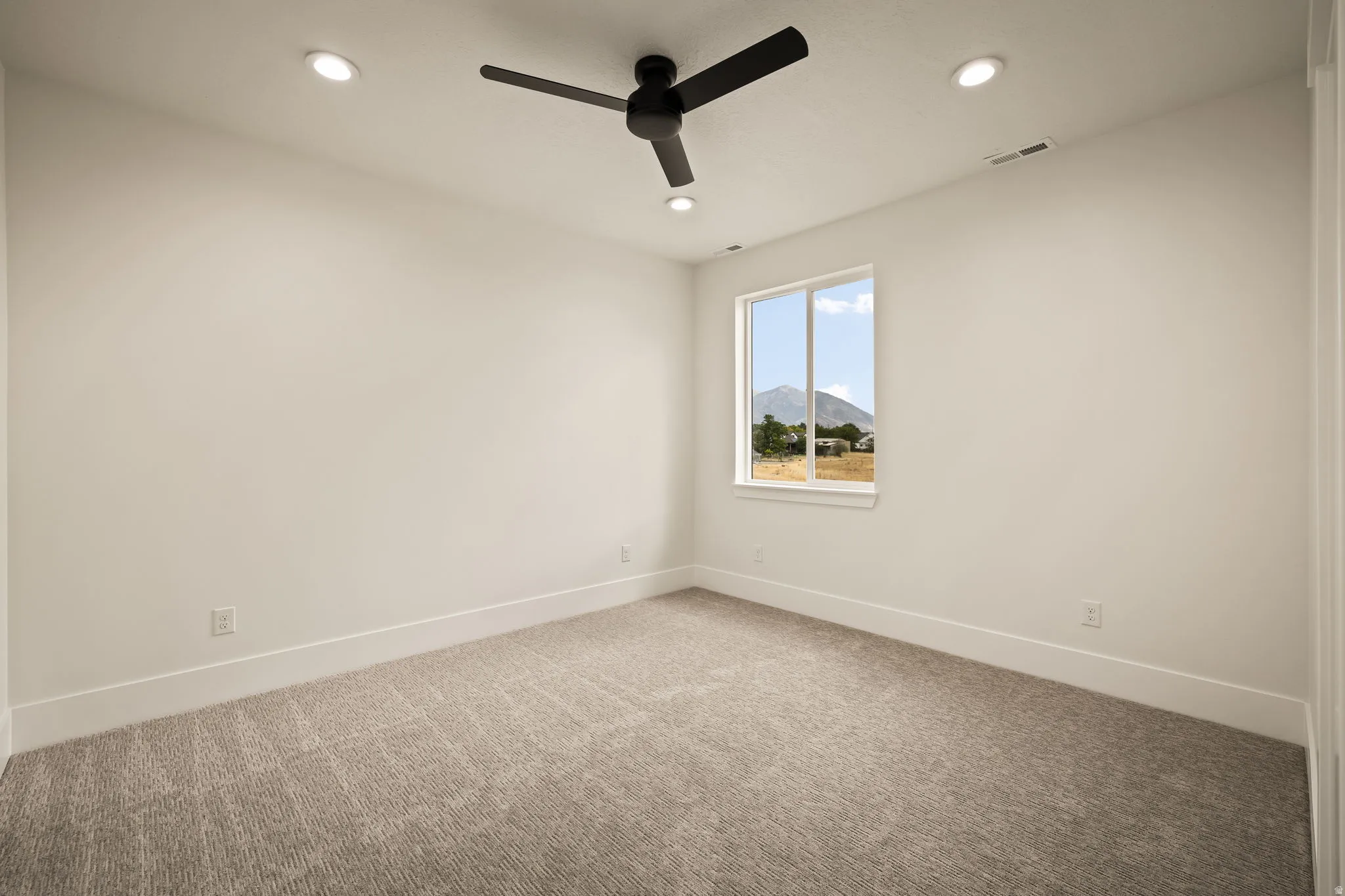 Neutral-toned carpeted room featuring a ceiling fan with integrated lighting, recessed ceiling lights, and a window framing a distant mountain landscape
