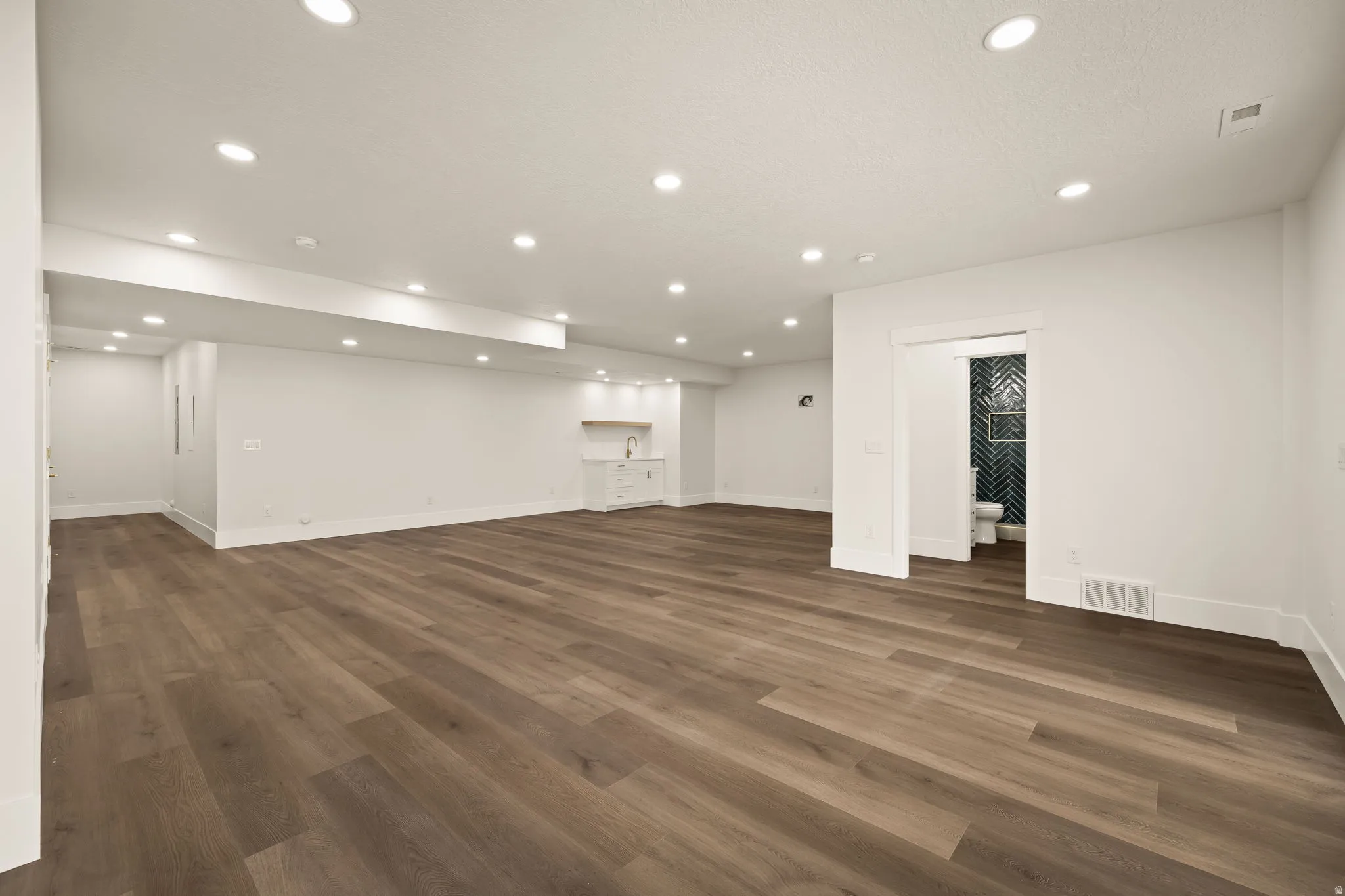 Expansive room featuring wood-finish flooring, recessed lighting, and white baseboards