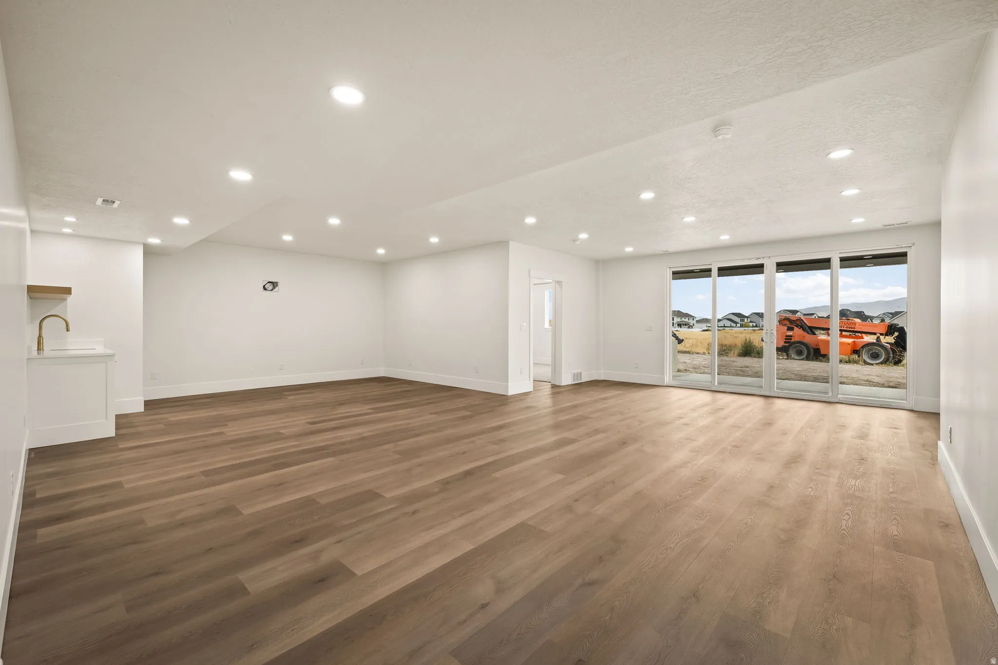 Spacious room featuring wood-finish flooring, recessed lighting, and a built-in wet bar with a gold-finish faucet
